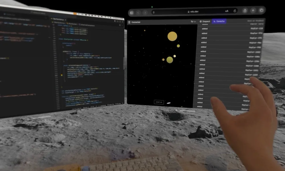 A virtual reality setup shows a coding environment with two screens on a simulated lunar surface. The left screen displays JavaScript code, while the right screen shows a web application with floating yellow spheres and a console log. A hand is extended towards the right screen, interacting with the interface.